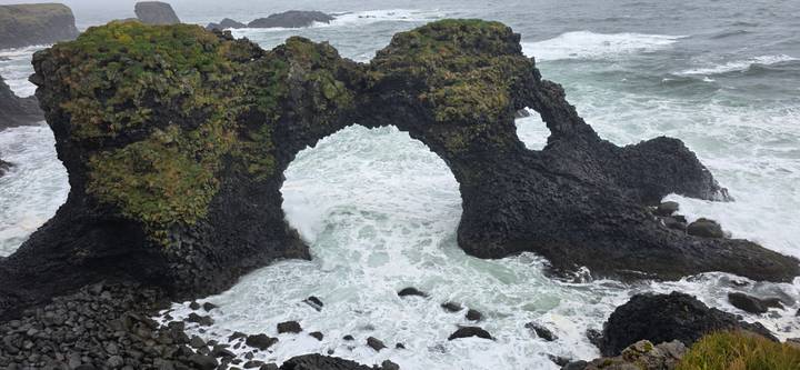 Natural volcanic rock arch over crashing waves along a rugged coastline