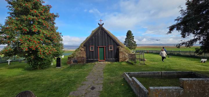 Tiny black-wood turf-roof church set in a green cemetery on a bright day