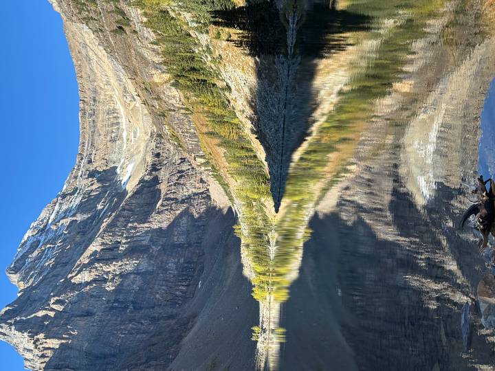 Crystal clear alpine lake perfectly mirroring steep rocky mountain walls under a blue sky