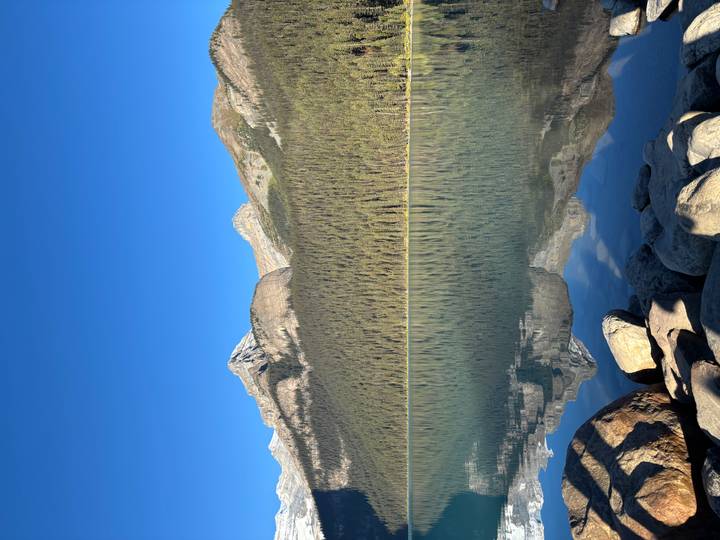 Wide tranquil lake with rocky shoreline and dense conifer forest beneath towering peaks