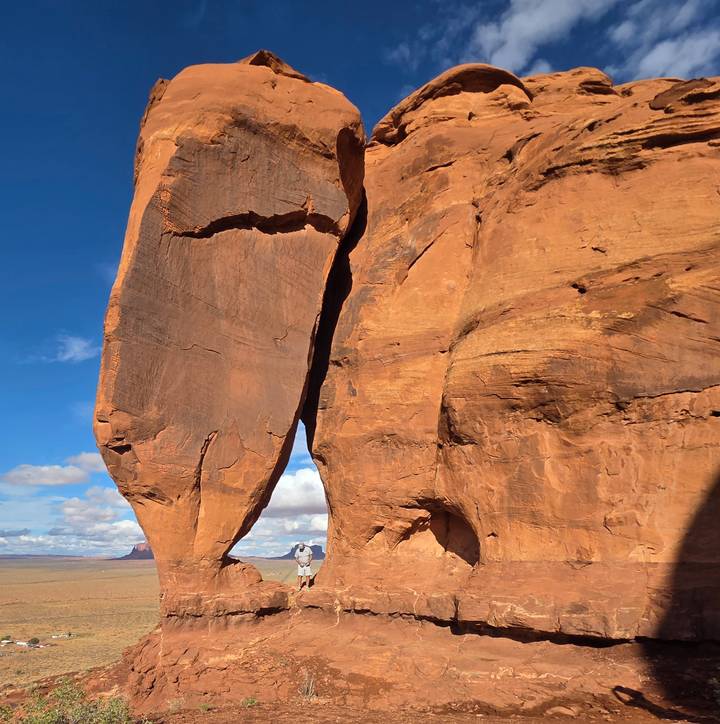 A massive sandstone fin split by a dramatic crack rises against a bright blue sky in the Utah desert.