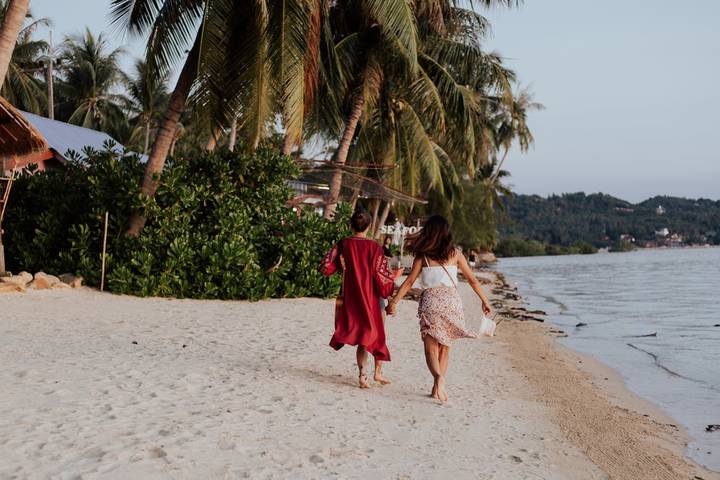 Two women holding hands while strolling along a tropical sand beach at dusk
