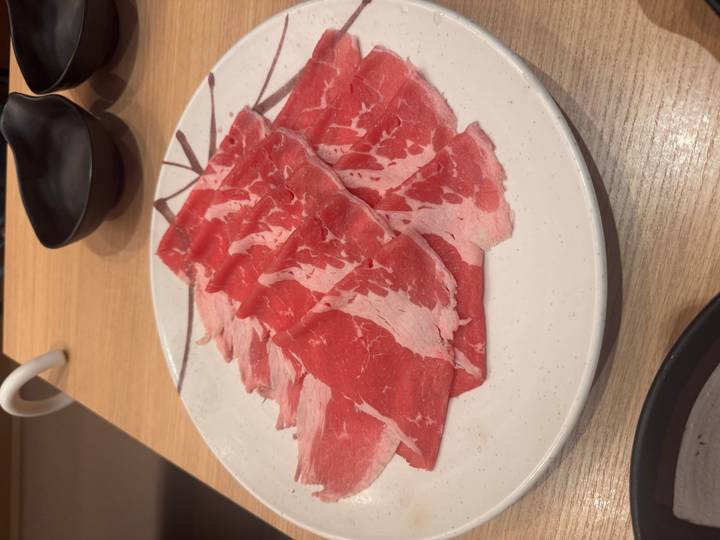 Plate of thinly sliced raw beef prepared for hot pot on a restaurant table.