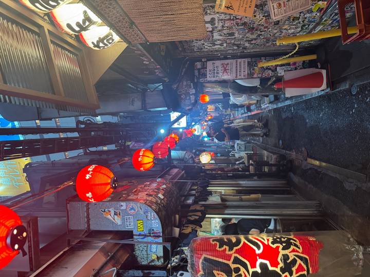 Narrow alleyway lined with tiny eateries and red lanterns, bustling with evening diners in Tokyo.