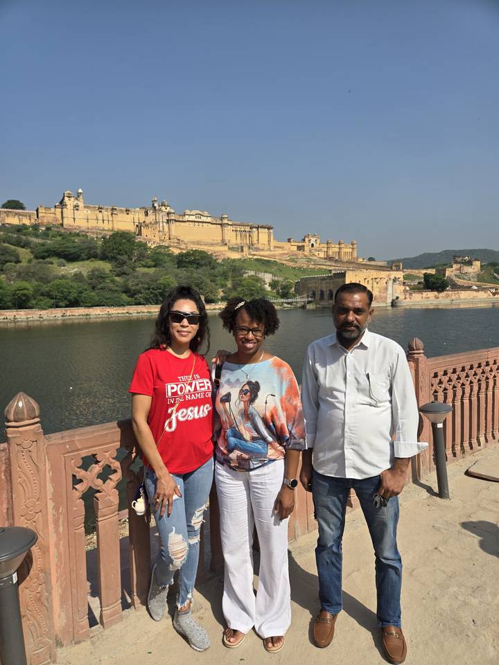 Travelers smile with Amber Fort and its reflecting lake in the bright morning sun.