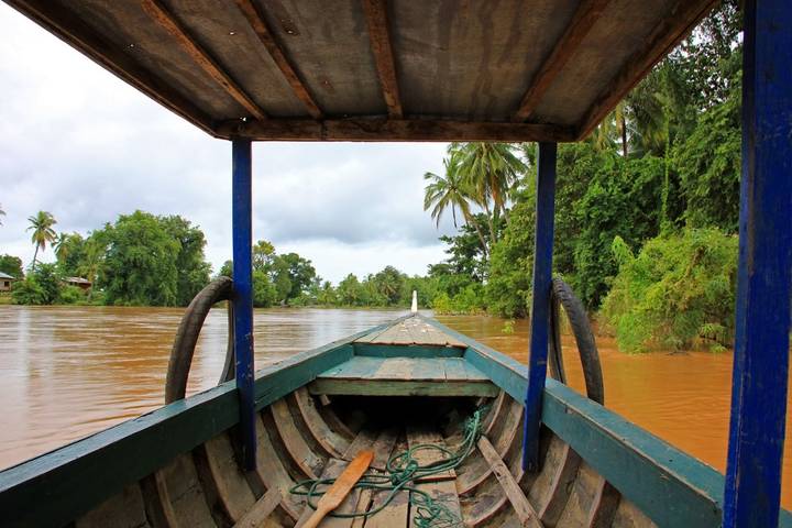 View from inside a wooden riverboat gliding along a muddy tropical river lined with palms