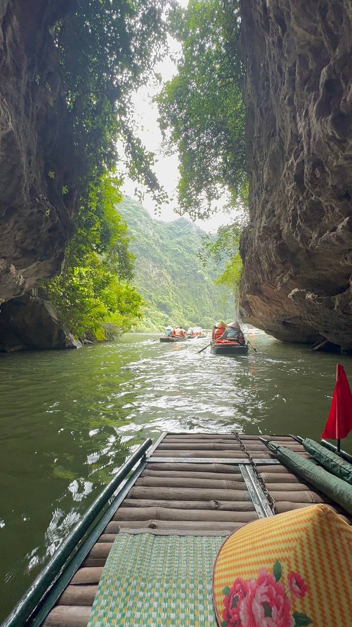 Rowboats with conical-hat rowers glide through a river canyon of lush karst cliffs