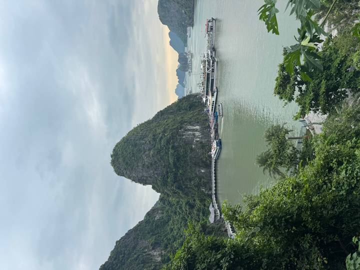 Quiet harbor with limestone karst backdrop and anchored boats beneath grey sky
