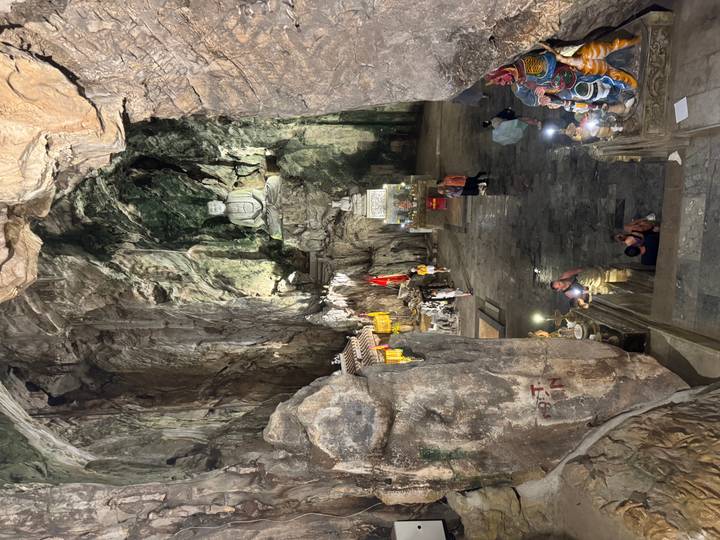 Dimly lit cave temple with large Buddha statue carved into rugged limestone chamber