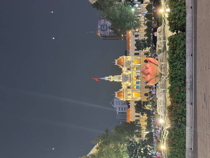 Night view of the illuminated Ho Chi Minh City Hall behind a lotus-shaped fountain, with crowds enjoying the plaza.