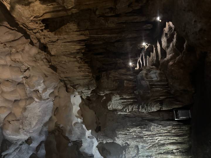 Dimly lit limestone cave interior with stalactites, stalagmites and a narrow staircase illuminated by small lamps.
