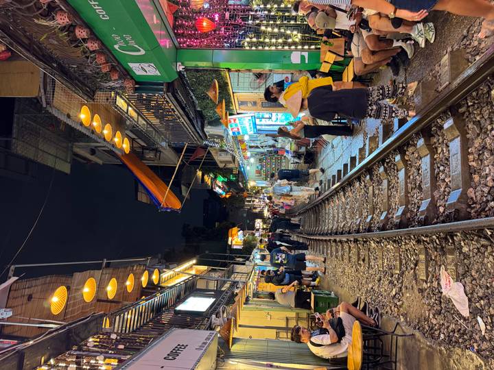 Lively Hanoi Train Street at night with patrons sitting beside railway tracks lined by cafes and lanterns.