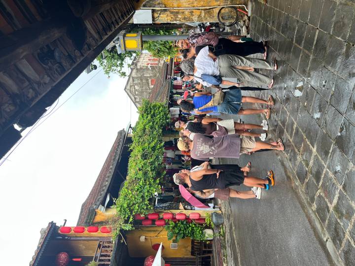 Tour group gathers on a wet stone street lined with lanterns and market stalls in Hoi An Old Town.