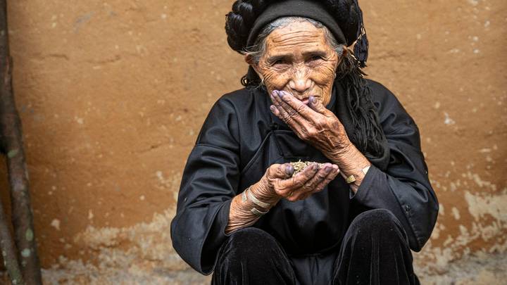 Portrait of an elderly woman in traditional black attire thoughtfully holding dried beans.