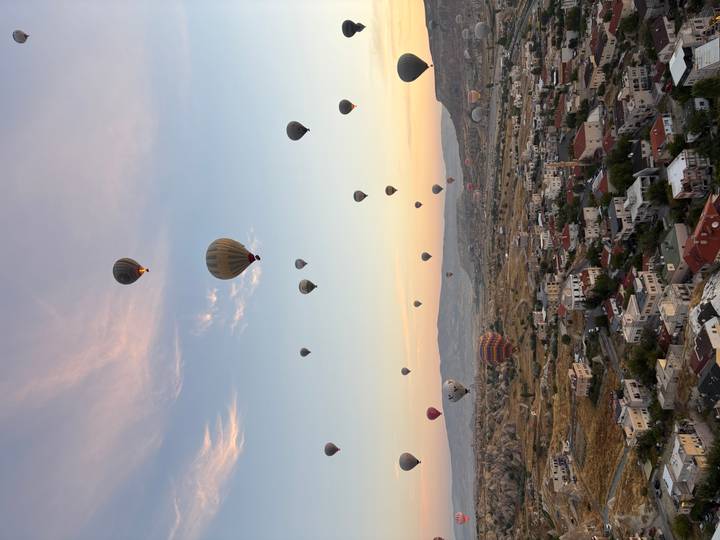 Dozens of colorful hot-air balloons drift over Cappadocia’s rocky landscape at sunrise.