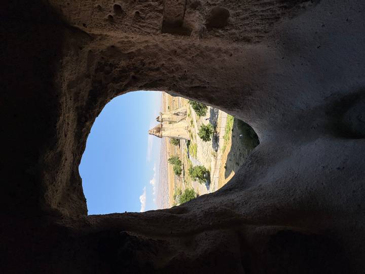 View through a natural rock window framing Cappadocia’s iconic fairy-chimney rock formations under a bright blue sky.