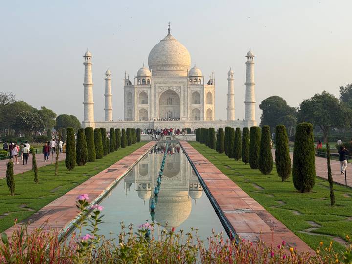 Iconic Taj Mahal reflected in a long pool with tourists lining the garden pathway