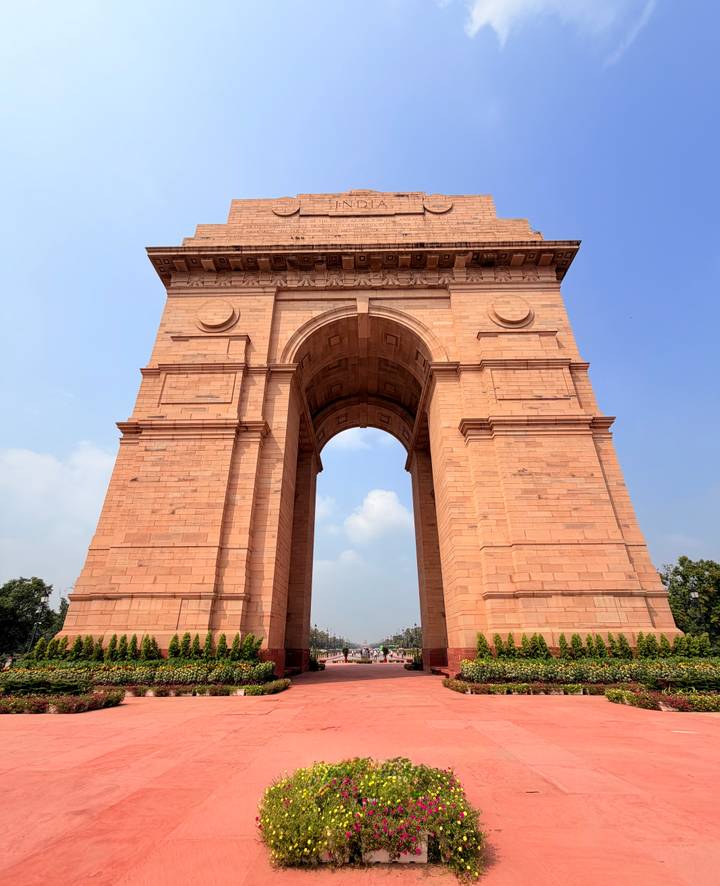 Massive sandstone India Gate monument reaching into a blue sky with soft clouds