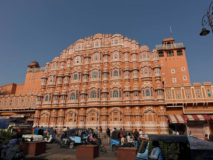 The pink façade of Jaipur's Hawa Mahal rising against a clear blue sky with city traffic below