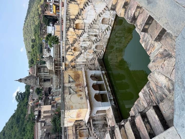 Historic step-well and temple complex with green water pool set among hills