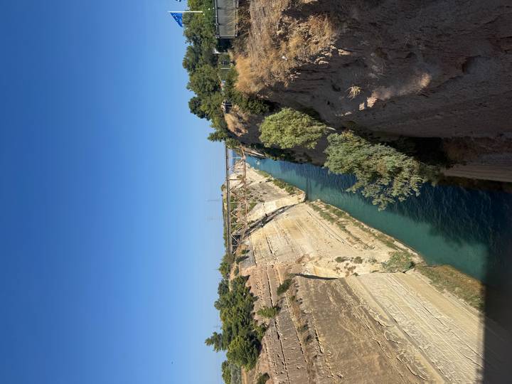 Deep turquoise waters of the Corinth Canal cutting between steep limestone walls under a clear sky.