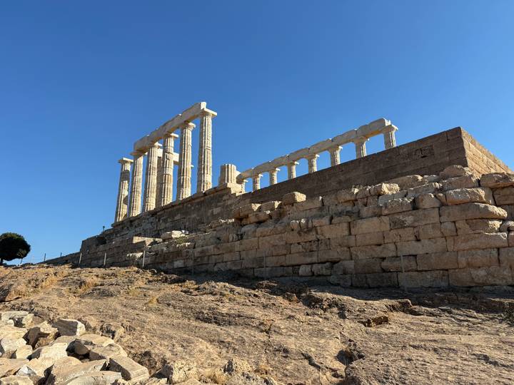 Ruins of the Temple of Poseidon at Cape Sounio rising over rugged rocks and blue sky.