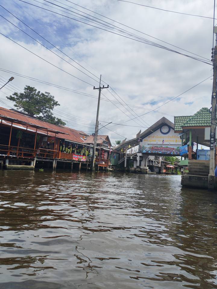 Canal entrance with wooden houses on stilts and sign reading 'Welcome to' above the water under cloudy sky