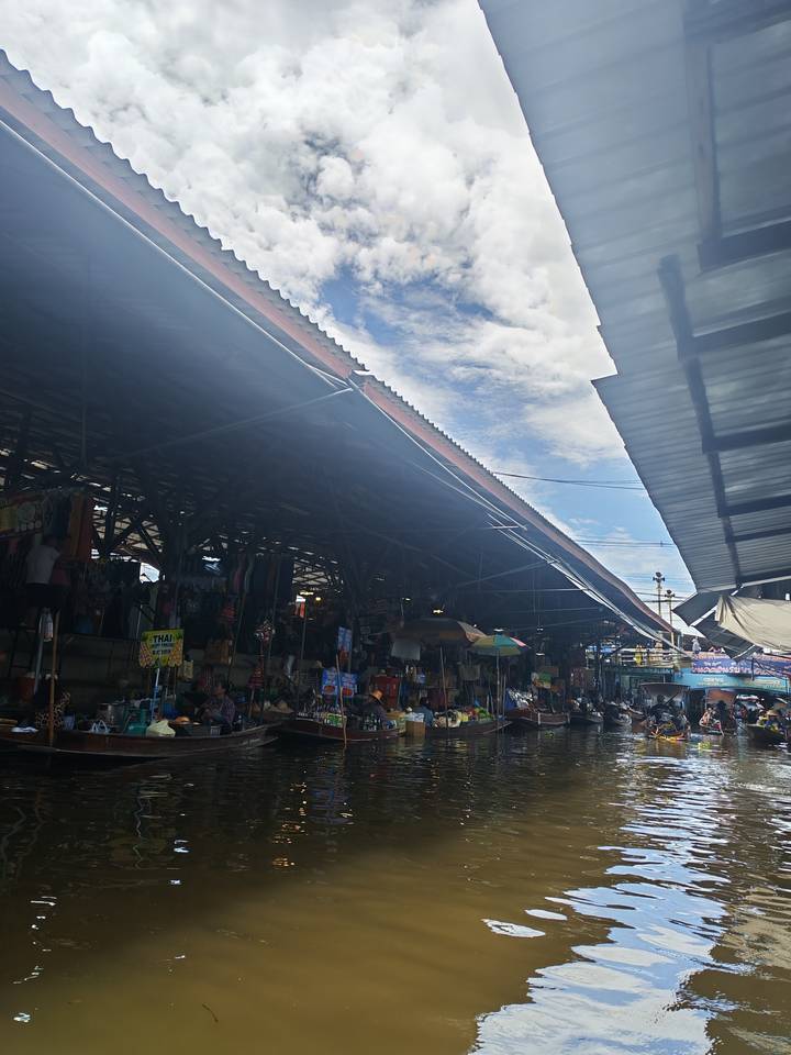 Roof structures and market stalls at floating market with strong glare and haze