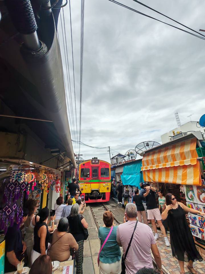Colorful train moving through Maeklong Railway Market with vendors and visitors close to tracks