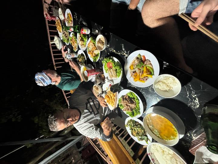 Dinner scene with two men and large spread of Vietnamese dishes on black table at night