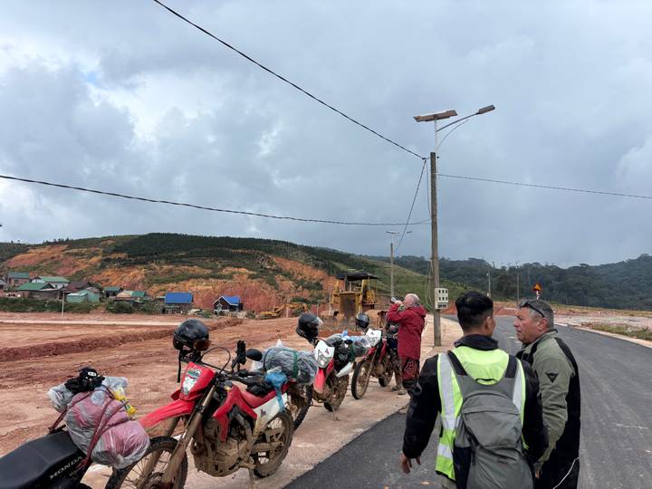 Group of riders with packed motorbikes stopped at roadside construction near red earth hills