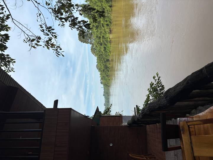 Serene view of wide brown river bordered by lush green forest taken from wooden balcony