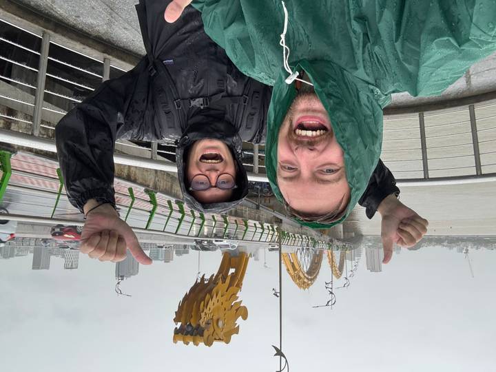 Two travellers in rain jackets celebrating at Dragon Bridge in Da Nang during heavy rain
