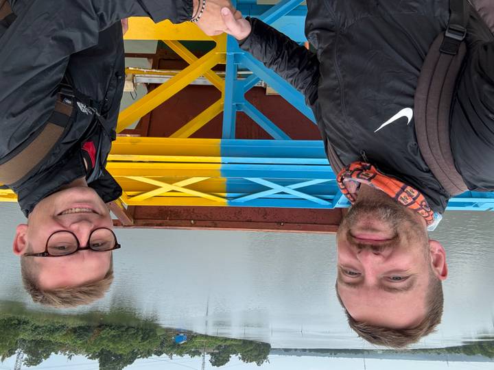 Two men posing on brightly painted blue and yellow bridge over calm water