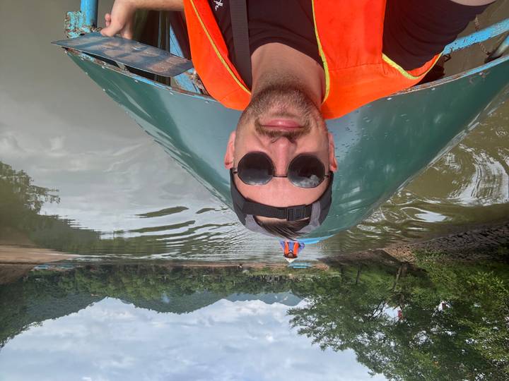 Selfie of traveller wearing lifevest and sunglasses on boat ride along calm river with karst hills in distance