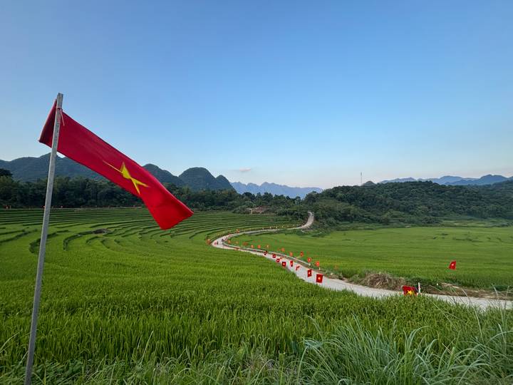 Vietnamese flag waves over vibrant rice terraces and a winding country road against a backdrop of karst hills at dusk
