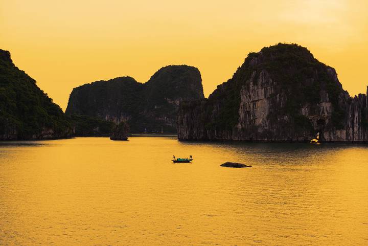 Golden dusk casts silhouettes of karst islets and a small boat in Ha Long Bay.