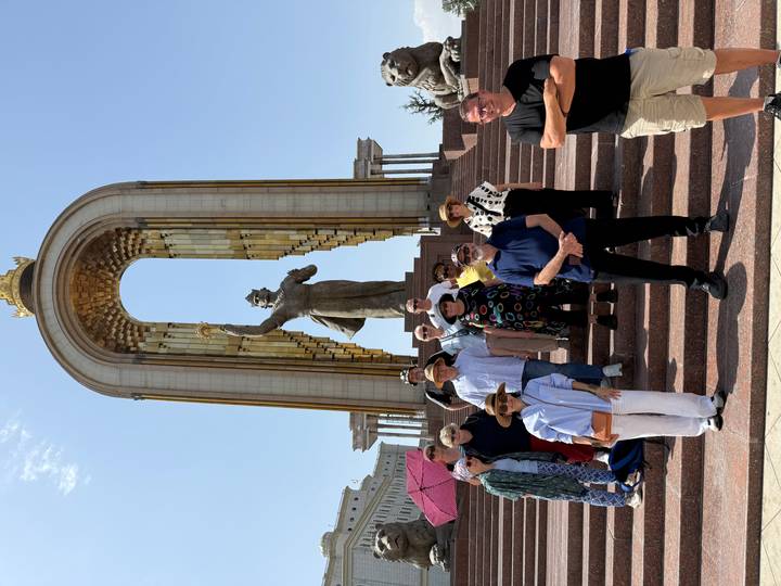 Tour group gathers on steps beneath the golden-arched Ismaili Somoni Monument in Dushanbe under clear skies.