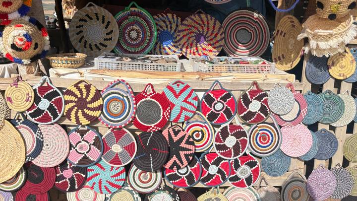 Sunlit market stall displaying rows of colourful woven basket lids and trays in geometric patterns.