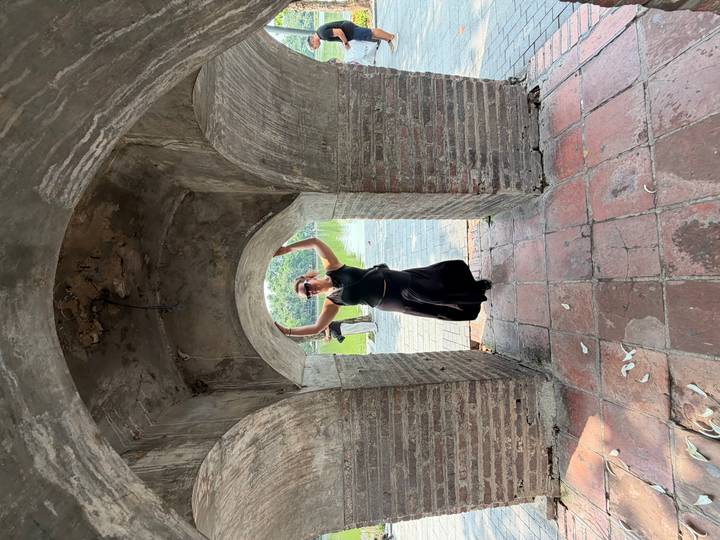 Woman jumps playfully under a stone archway of an ancient gate beside a calm lake.