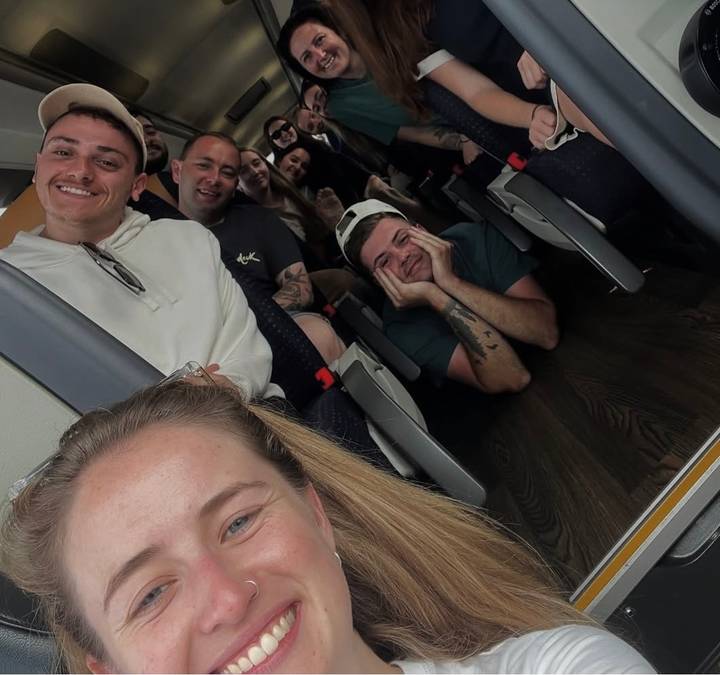 Playful selfie of a group of young travellers seated inside a tour bus.