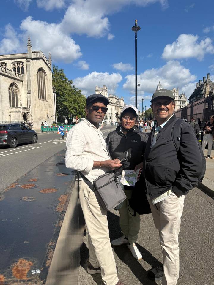 Three men standing on a London street near Westminster buildings on a sunny day.