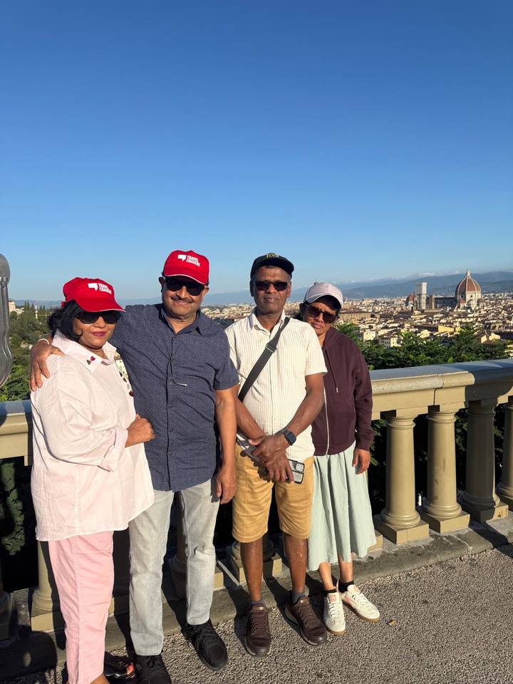 Group wearing red caps posing at Florence overlook with Duomo in background.