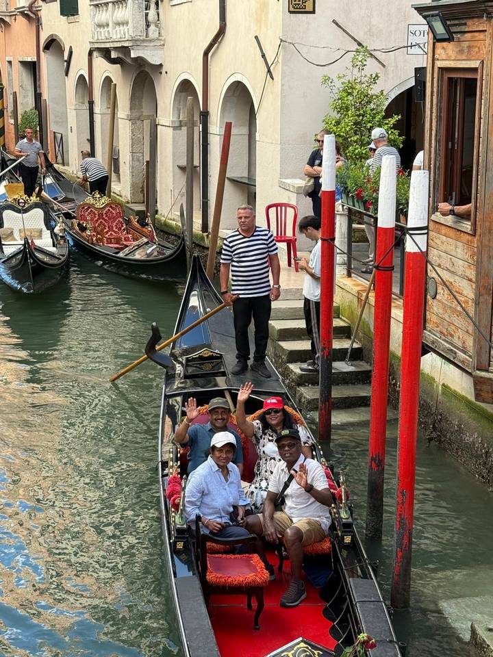 Gondolier steering gondola with waving passengers through a Venice canal.