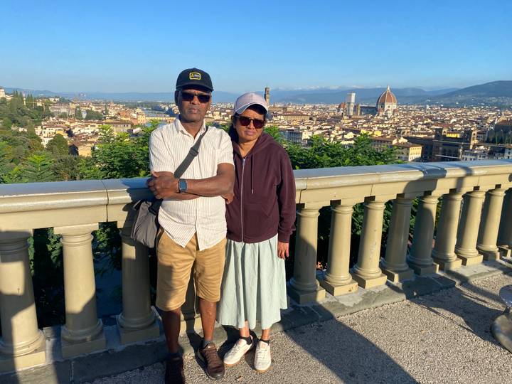 A couple stands at a scenic terrace overlooking Florence with the iconic Duomo and cityscape spread out beneath a clear blue sky.