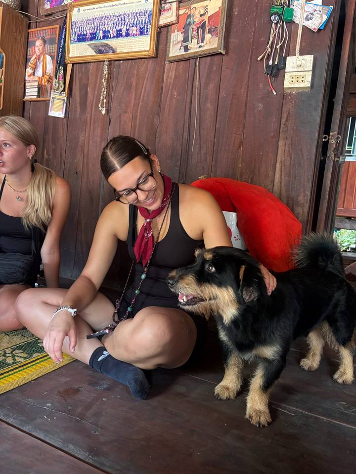 Traveler smiles while petting a friendly black dog inside a rustic wooden hut.