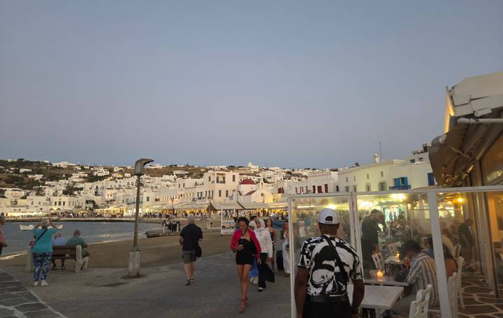Evening crowds wander the harborfront street lined with whitewashed Mykonos buildings and cafés.