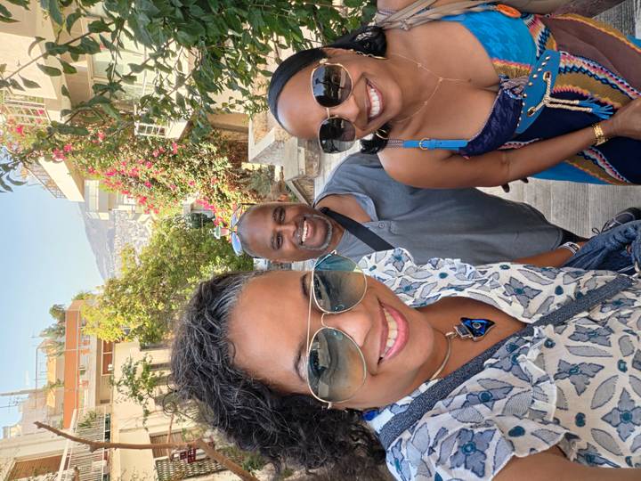 Three friends wearing sunglasses smile on a steep Athens staircase framed by bougainvillea.