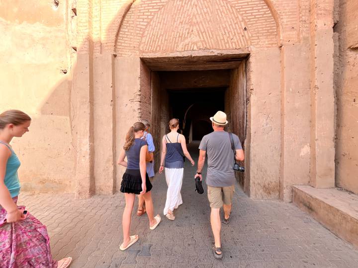 Travellers walk toward a dark tunnel entrance in a mud-brick fortress.