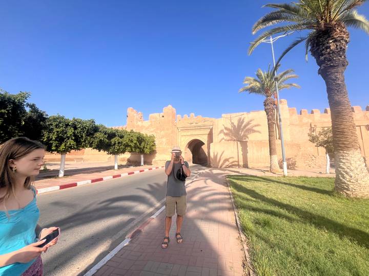 A photographer captures an image of a companion in front of an arched gate and palm shadows.